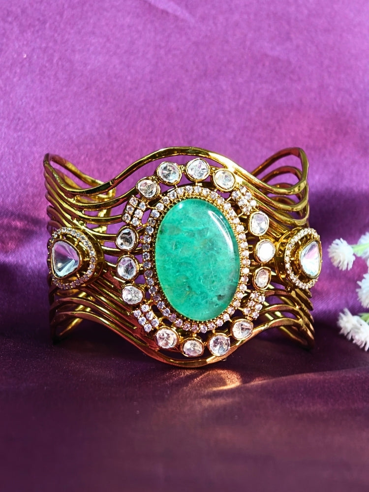 The Mariam Mint Green Bracelet (Adjustable) features an intricate wavy gold design with a large oval mint green stone at the center, accented by small kundan stones, and is displayed on a purple satin backdrop—ideal for elegant wedding ensembles.