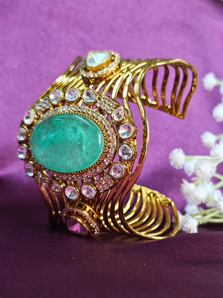 The Mariam Mint Green Bracelet (Adjustable) features an intricate wavy gold design with a large oval mint green stone at the center, accented by small kundan stones, and is displayed on a purple satin backdrop—ideal for elegant wedding ensembles.