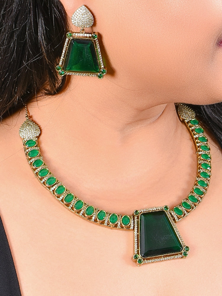 A woman wears the Marley Green Necklace Set, featuring a gold necklace with round emerald green stones and a large green pendant, paired with matching green and gold earrings in a bold triangular design.