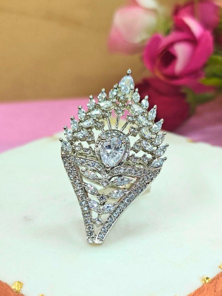 The Marlow Ring, a large adjustable piece adorned with pear-shaped and round American Diamond stones, is showcased on a white surface with softly blurred pink roses in the background.  Perfect American Diamond cocktail ring. 