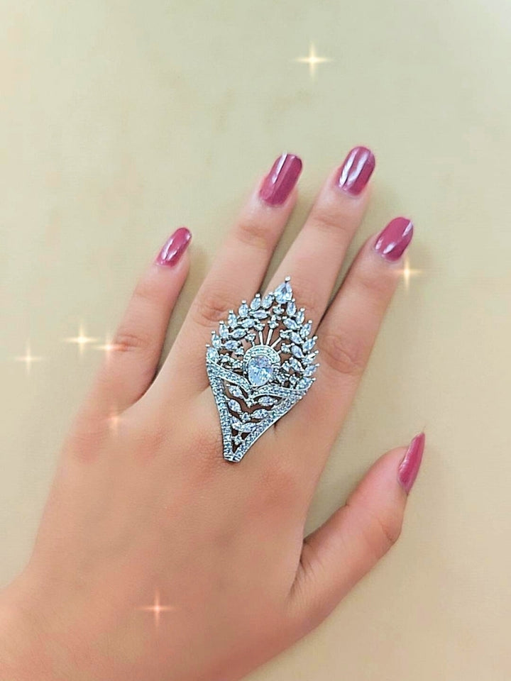 The Marlow Ring, a large adjustable piece adorned with pear-shaped and round American Diamond stones, is showcased on a white surface with softly blurred pink roses in the background.  Perfect American Diamond cocktail ring. 