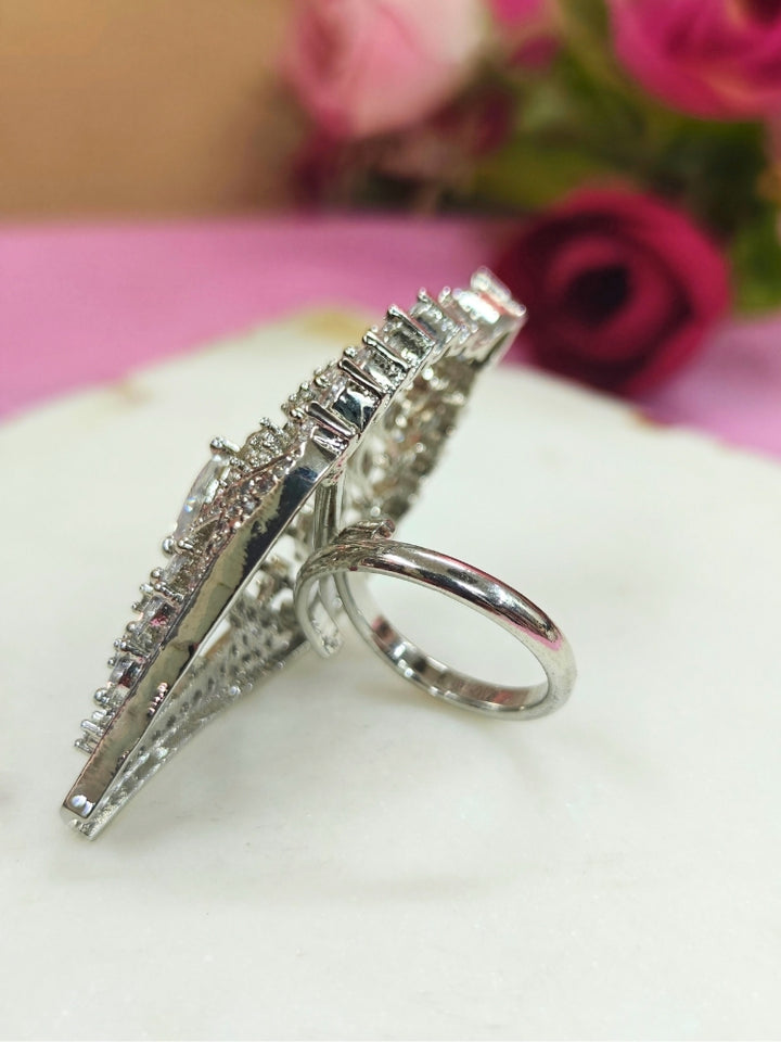 The Marlow Ring, a large adjustable piece adorned with pear-shaped and round American Diamond stones, is showcased on a white surface with softly blurred pink roses in the background.  Perfect American Diamond cocktail ring. 