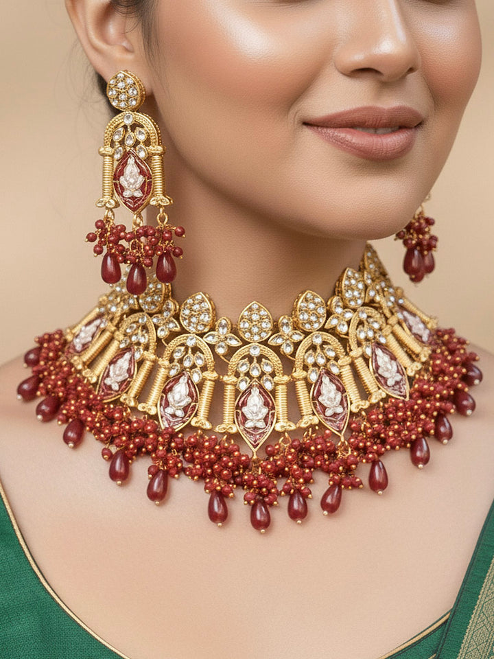 Close-up of a woman wearing an ornate traditional (Gold Polish) Maroon Choker jewellery set and earrings and maangtikka with Kundan, Meenakari, Crystal beads and Tumble beads. Close-up of intricate Kundan craftsmanship in artificial bridal jewelry. Bride wearing a traditional Kundan artificial necklace set for her wedding ceremony.