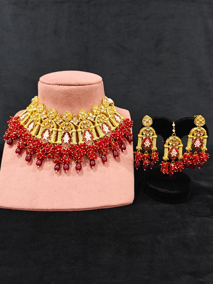 Close-up of an ornate traditional (Gold Polish) Maroon Choker jewellery set and earrings and maangtikka with Kundan, Meenakari, Crystal beads and Tumble beads. Close-up of intricate Kundan craftsmanship in artificial bridal jewelry. A traditional Kundan artificial necklace set for her wedding ceremony.