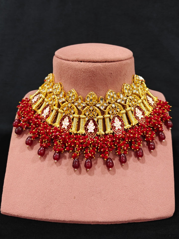 Close-up of an ornate traditional (Gold Polish) Maroon Choker jewellery set and earrings and maangtikka with Kundan, Meenakari, Crystal beads and Tumble beads. Close-up of intricate Kundan craftsmanship in artificial bridal jewelry. A traditional Kundan artificial necklace set for her wedding ceremony.