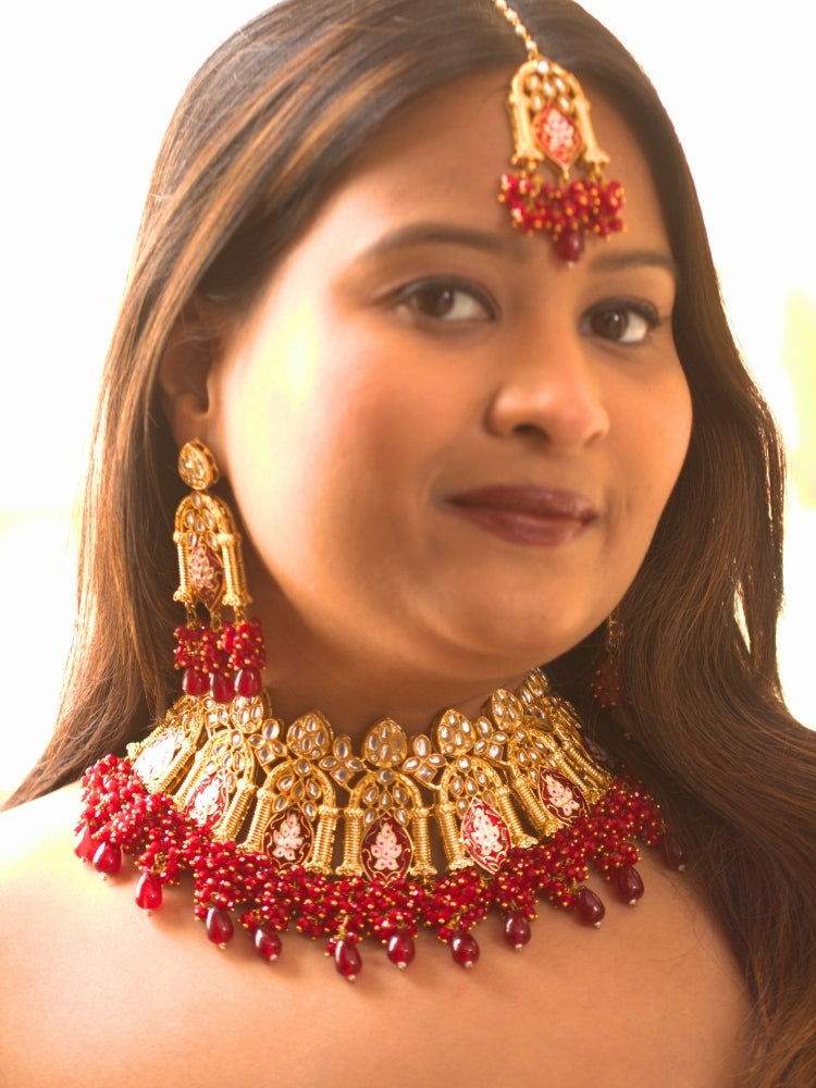 Close-up of a woman wearing an ornate traditional (Gold Polish) Maroon Choker jewellery set and earrings and maangtikka with Kundan, Meenakari, Crystal beads and Tumble beads. Close-up of intricate Kundan craftsmanship in artificial bridal jewelry. Bride wearing a traditional Kundan artificial necklace set for her wedding ceremony.