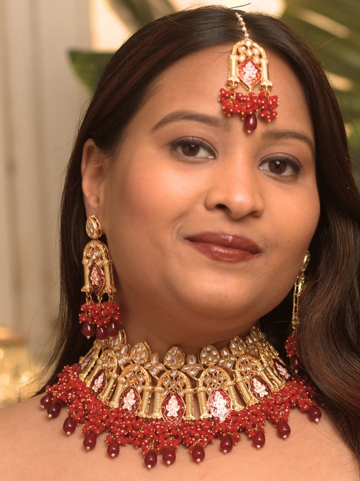 Close-up of a woman wearing an ornate traditional (Gold Polish) Maroon Choker jewellery set and earrings and maangtikka with Kundan, Meenakari, Crystal beads and Tumble beads. Close-up of intricate Kundan craftsmanship in artificial bridal jewelry. Bride wearing a traditional Kundan artificial necklace set for her wedding ceremony.