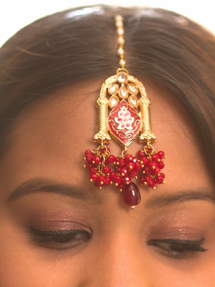 Close-up of a woman wearing an ornate traditional (Gold Polish) Maroon Choker jewellery set and earrings and maangtikka with Kundan, Meenakari, Crystal beads and Tumble beads. Close-up of intricate Kundan craftsmanship in artificial bridal jewelry. Bride wearing a traditional Kundan artificial necklace set for her wedding ceremony.