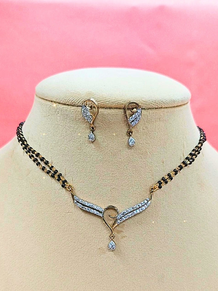 Meenakshi Mangalsutra—a gold necklace with black mangalsutra beads and matching earrings, pendant featuring sparkling American Diamonds—set against a cream dummy, perfect for your wedding ceremony dress. Diamond mangalsutra. Modern mangalsutra. 