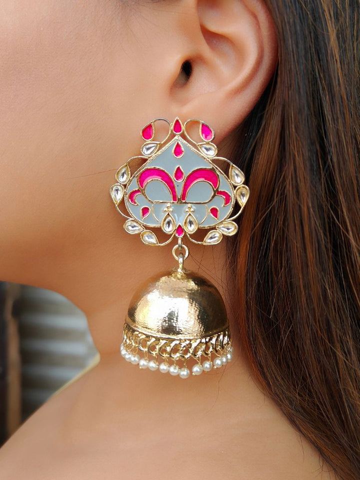 A close-up of a womans ear wearing Megha Earrings, large traditional gold jhumkas with Meenakari work, Kundan detailing, and dome-shaped design adorned with small hanging pearls.
