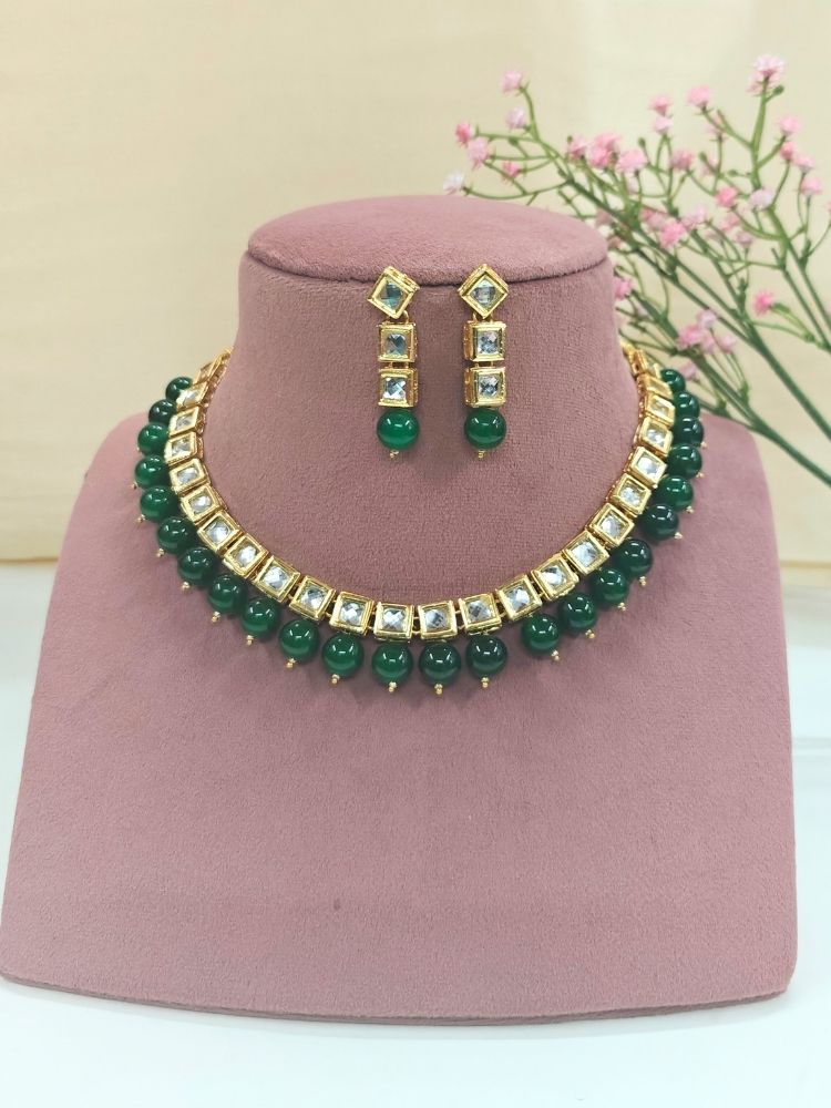 The Green Necklace Set, featuring gold and white Kundan stones with large Green beads and matching square earrings, is displayed on a pink dummy. 