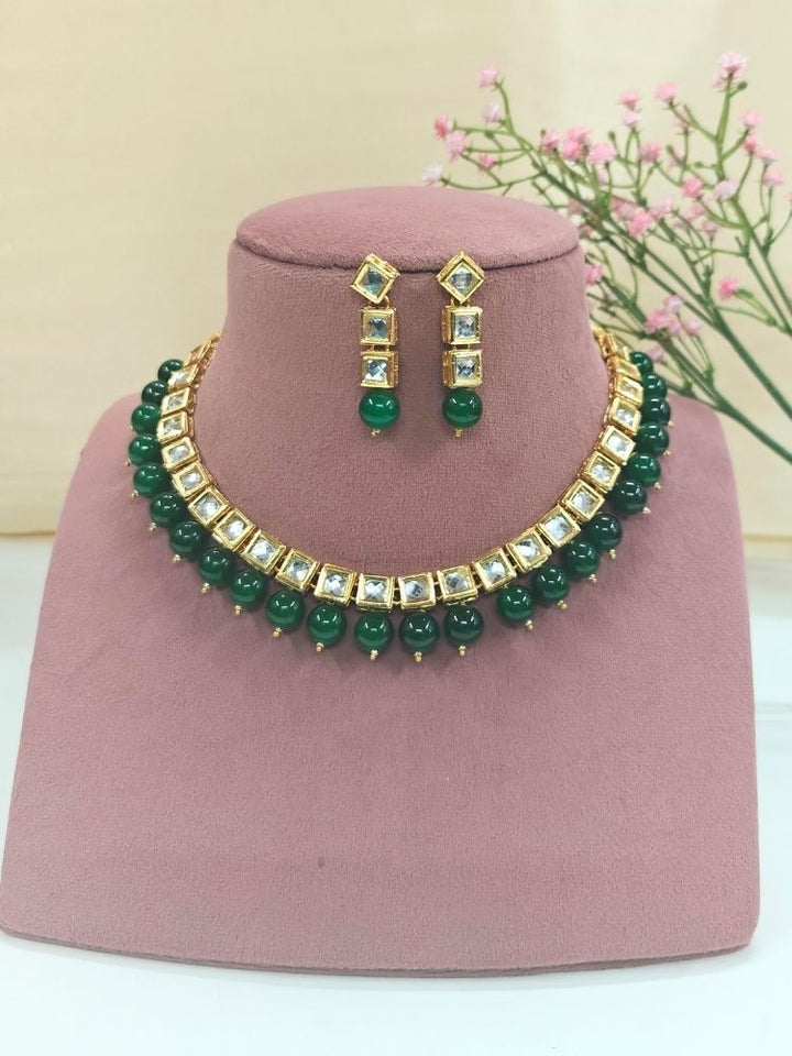 The Green Necklace Set, featuring gold and white Kundan stones with large Green beads and matching square earrings, is displayed on a pink dummy. 