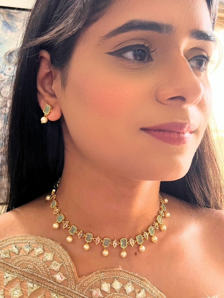 Close-up of a woman wearing the Mint Green Amelia Choker Necklace adorned with colored gemstones and dangling pearls, matching earrings, and a Mint Green top—an elegant choice for wedding ceremonies. Her lips are lightly colored, with dark hair partially visible.