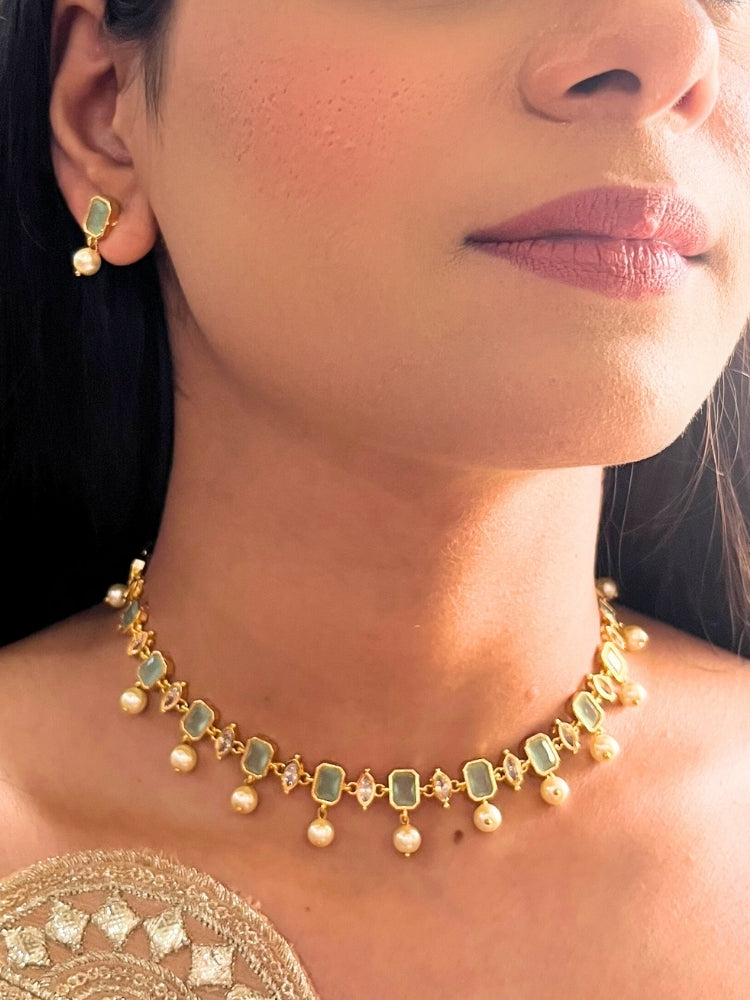 Close-up of a woman wearing the Mint Green Amelia Choker Necklace adorned with colored gemstones and dangling pearls, matching earrings, and a Mint Green top—an elegant choice for wedding ceremonies. Her lips are lightly colored, with dark hair partially visible.