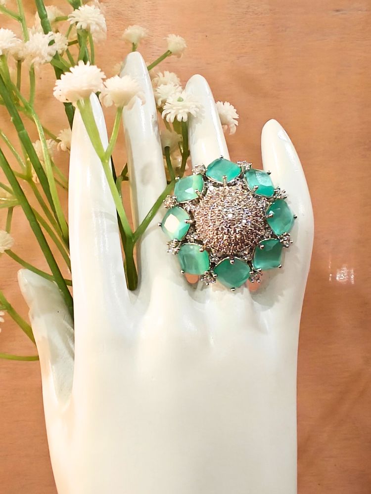 The Mint Green Aster Ring is a round silver piece with a sparkling, round-shaped center made with white American diamonds, surrounded by petal shaped Mint Green gemstones, along with an adjustable band. It’s shown on a White Hand Mannequin.