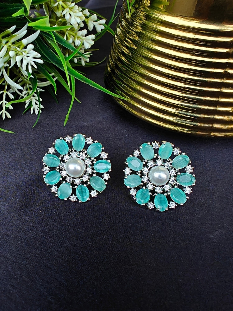 The Mint Green Blossom Earrings showcase a central white pearl encircled by alternating Mint Green stones and American diamonds, elegantly displayed on Black fabric with green leaves and a Golden Accent.