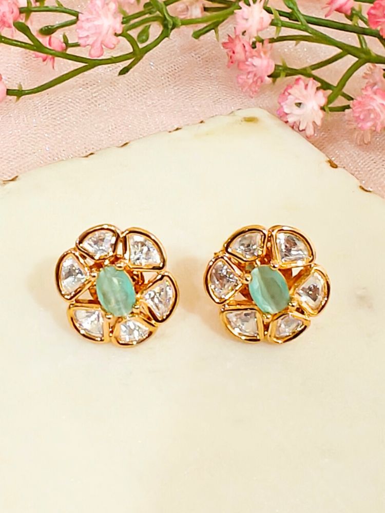 The Mint Green Daffodil stud Earrings feature gold flower-shaped brass settings with clear American Diamond petals and a mint green stone center, displayed on a white surface with sheer white fabric in the background.