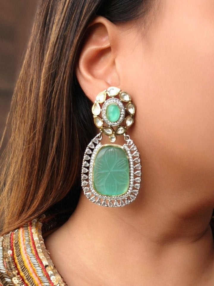 A close-up of a womans ear wearing Mint Green Fiona Earrings featuring an Mint Green carved stone, ornate American Diamonds and Kundan. Her dark hair is partially visible, and she wears a colorful embroidered garment.