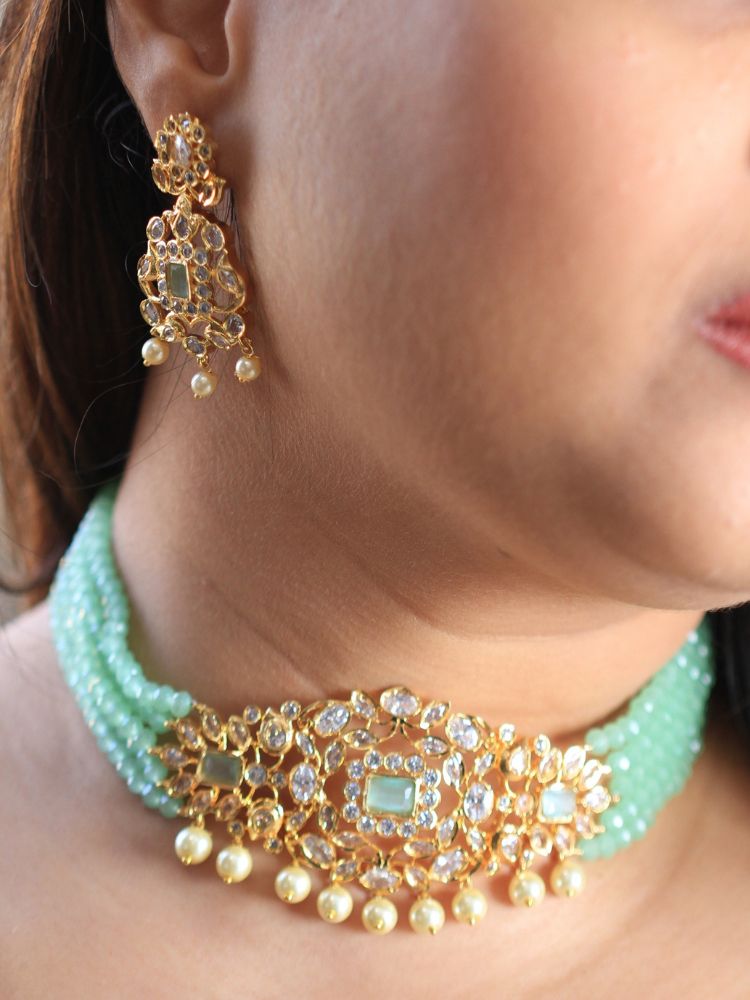 A woman with long brown hair wears the Mint Green Sarah chokerNecklace Set, featuring an ornate crystal-beaded choker with gold and pearl details and matching gold earrings. She has a neutral expression and wears a light-colored top.