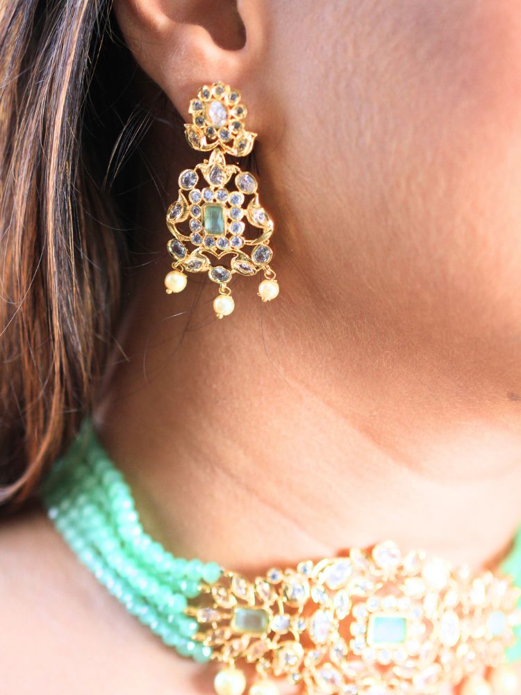 A woman with long brown hair wears the Mint Green Sarah chokerNecklace Set, featuring an ornate crystal-beaded choker with gold and pearl details and matching gold earrings. She has a neutral expression and wears a light-colored top.