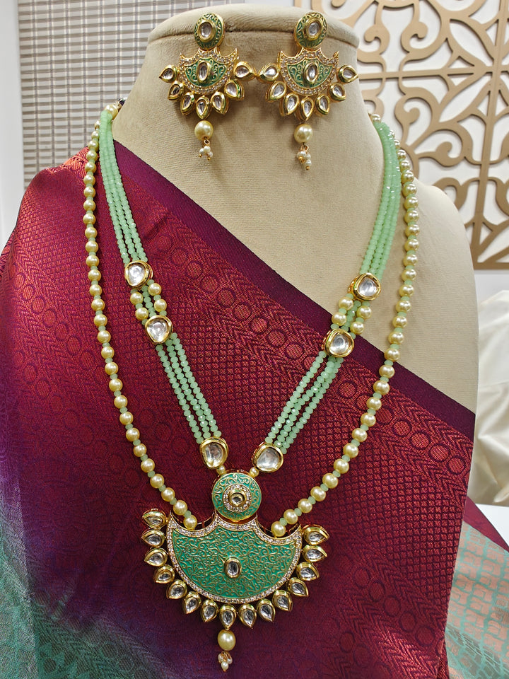 A mannequin in a in a deep red sari showcases the mint green Zareen Necklace Set, featuring gold and mint green tones with pearl accents, matching earrings, intricate designs, american diamonds, and elegant Kundan detailing.