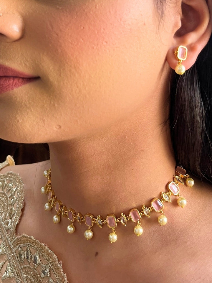 A girl looking at the camera wearing The Mint Pink Amelia Choker Necklace Set features mint pink colored stones and dangling pearls, with matching stud earrings. 
