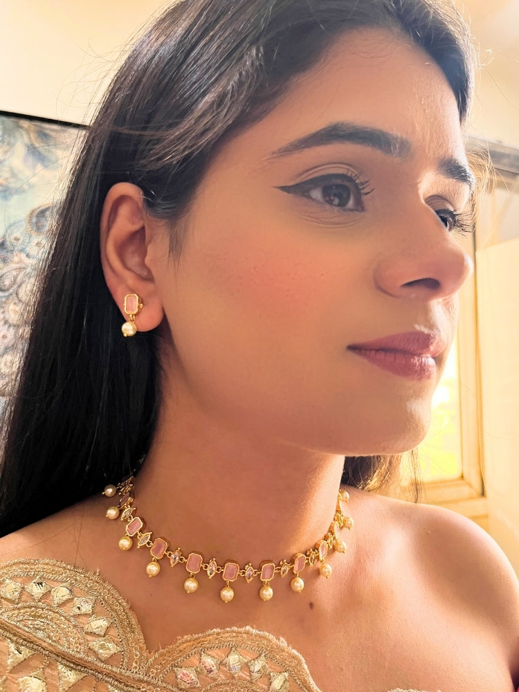 A girl looking at the camera wearing The Mint Pink Amelia Choker Necklace Set features mint pink colored stones and dangling pearls, with matching stud earrings. 