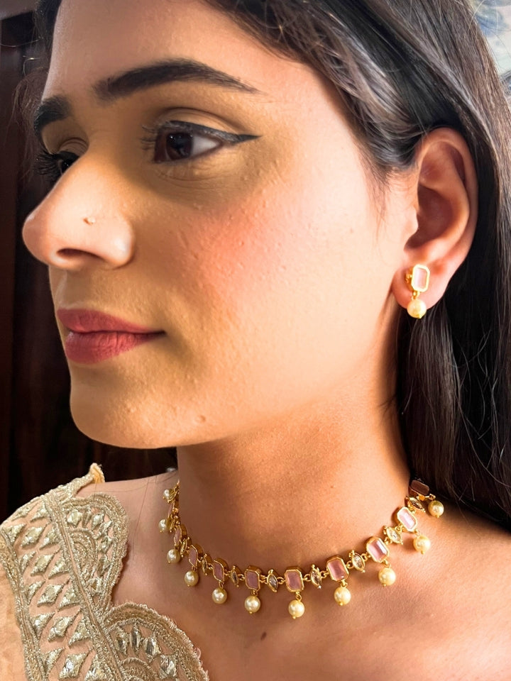 A girl looking at the camera wearing The Mint Pink Amelia Choker Necklace Set features mint pink colored stones and dangling pearls, with matching stud earrings. 