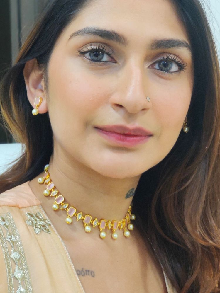A girl looking at the camera wearing The Mint Pink Amelia Choker Necklace Set features mint pink colored stones and dangling pearls, with matching stud earrings. 