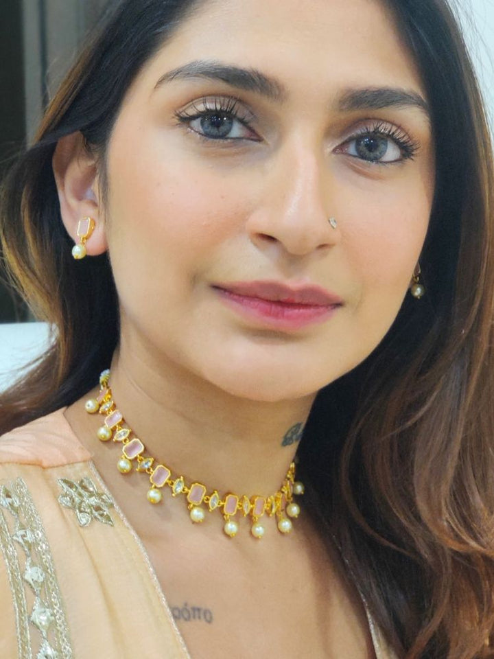 A girl looking at the camera wearing The Mint Pink Amelia Choker Necklace Set features mint pink colored stones and dangling pearls, with matching stud earrings. 