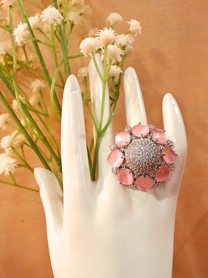The Mint Pink Aster Ring is a round silver piece with a sparkling, round-shaped center made with white American diamonds, surrounded by petal shaped Mint Pink gemstones, along with an adjustable band. It’s shown on a White Hand Mannequin.