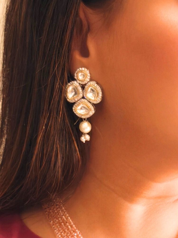 A woman wears the Mint Pink Blair Necklace Set, featuring multi-strand crystals and pearls necklace, along with bog round and square tyani kundan stones, surrounded by american diamonds, along with pearls hanging at the bottom to accentuate the over all look. The necklace comes with matching earrings. She pairs it with a maroon saree, matching earrings, and smiles with red lipstick, her face partially visible.