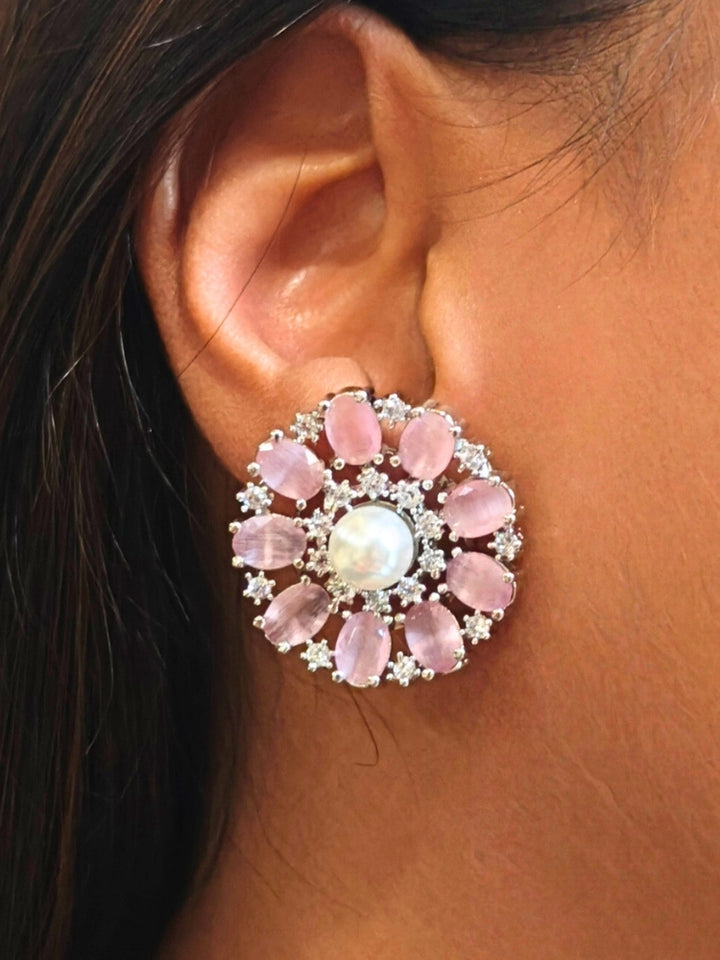 A close-up of a womans ear wearing the Mint Pink Blossom stud Earrings—large, circular Mint Pink earrings with a pearl at the center, colorful accents, and a border of sparkling American Diamonds. The stud earrings give a flower earrings feel. 