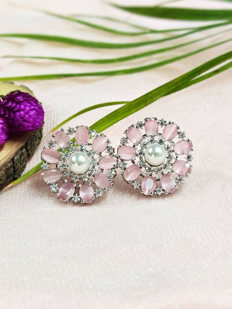 The Mint Pink Blossom Earrings showcase a central white pearl encircled by alternating Mint Pink stones and American diamonds, elegantly displayed on soft pink fabric with green leaves and a purple flower.