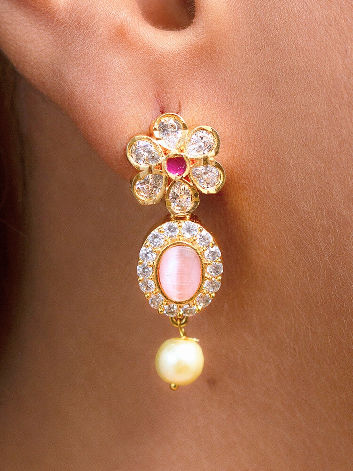 The Mint Pink Samrina Necklace Set entails multiple mint pink stones, surrounded by american diamonds, along with pearls hanging at the bottom.  Comes with matching earrings - is showcased on a black surface, with a patterned cup of crystals and yellow, white, and green artificial flowers in the background.