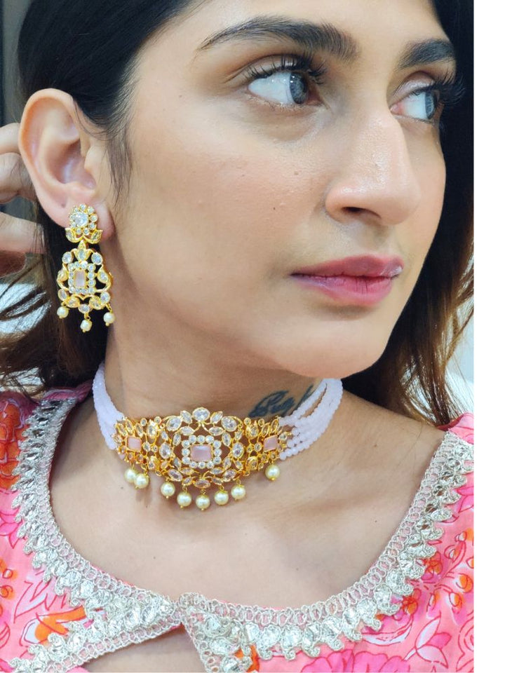 A woman with long brown hair wears the Mint Pink Sarah choker Necklace Set, featuring an ornate crystal-beaded choker with gold and pearl details and matching gold earrings. She has a neutral expression and wears a light-colored top.