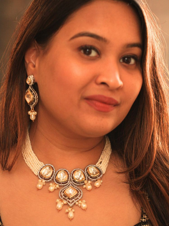 A woman with long brown hair wears the Moissanite & Pearl Reema Necklace Set, featuring multiple strands of pearls, along with kundan moissanite, surrounded by american diamonds, with hanging pearls, along with matching earrings. She smiles softly, her makeup flawless, while the background remains gently blurred. Kundan necklace. Moissanite necklace.