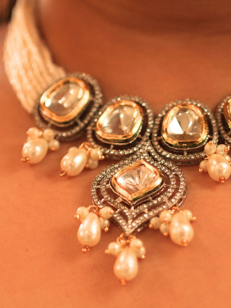 A woman with long brown hair wears the Moissanite & Pearl Reema Necklace Set, featuring multiple strands of pearls, along with kundan moissanite, surrounded by american diamonds, with hanging pearls, along with matching earrings. She smiles softly, her makeup flawless, while the background remains gently blurred. Kundan necklace. Moissanite necklace.