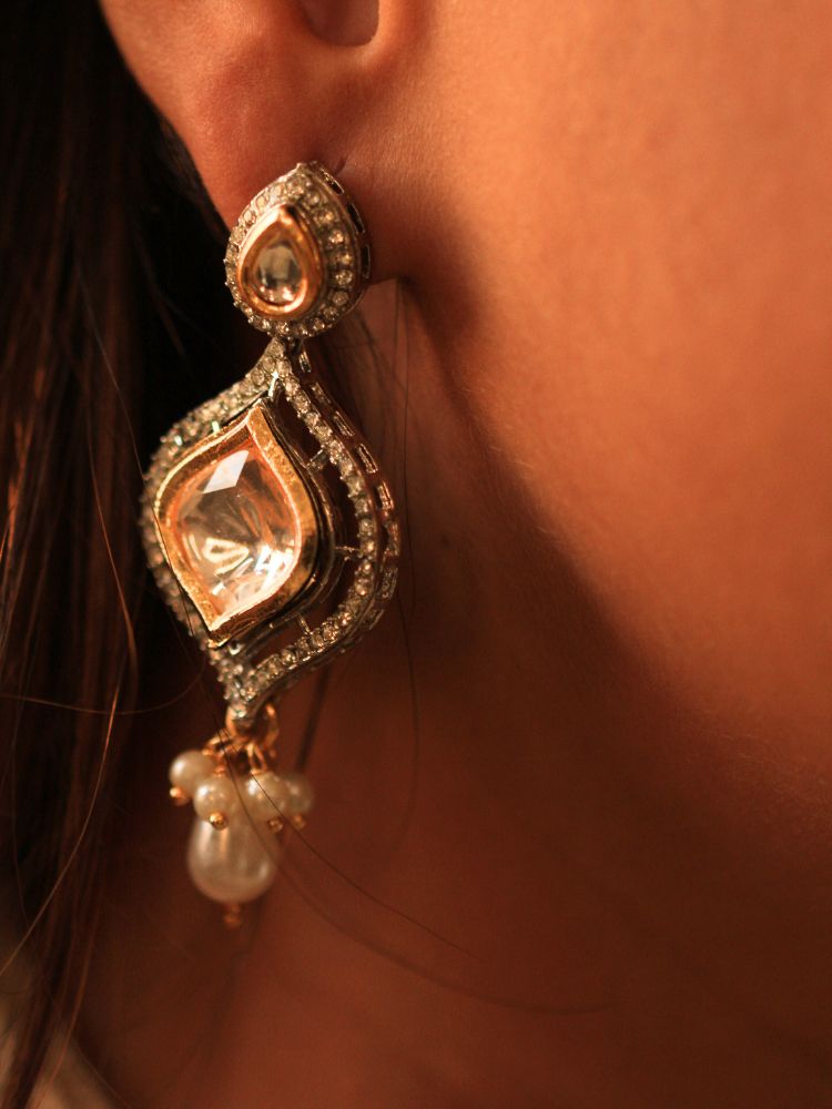A woman with long brown hair wears the Moissanite & Pearl Reema Necklace Set, featuring multiple strands of pearls, along with kundan moissanite, surrounded by american diamonds, with hanging pearls, along with matching earrings. She smiles softly, her makeup flawless, while the background remains gently blurred. Kundan necklace. Moissanite necklace.