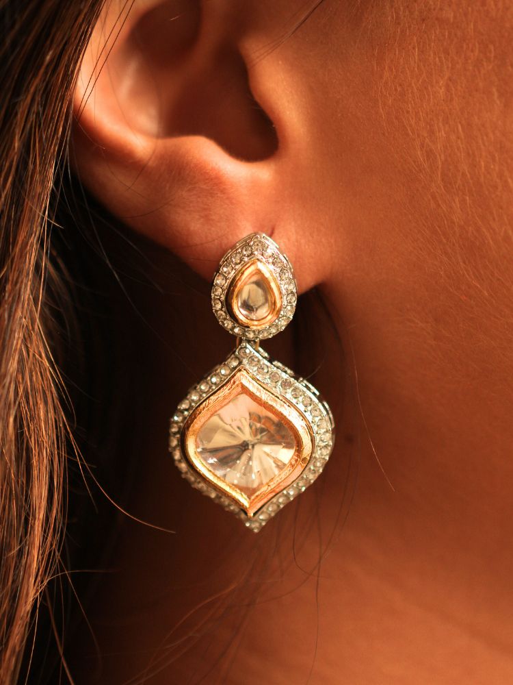 A woman with long dark hair wears the Moissanite Susan Necklace Set—gold and silver Kundan necklace surrounded by American Diamonds, with matching earrings—gazing neutrally at the camera, effortlessly highlighting this luxury jewelry.