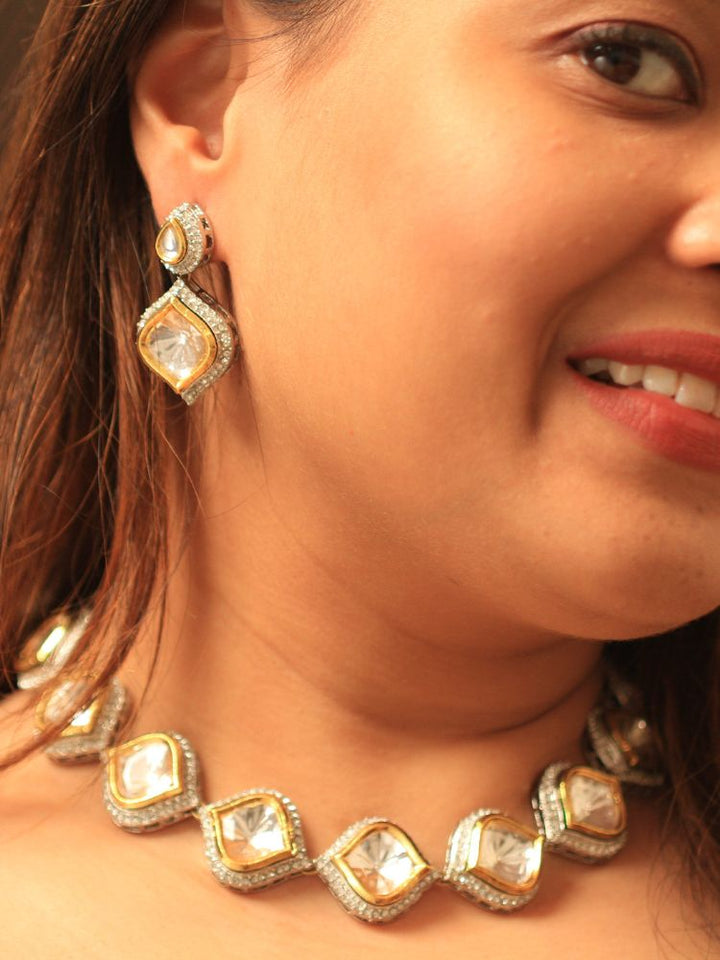 A woman with long dark hair wears the Moissanite Susan Necklace Set—gold and silver Kundan necklace surrounded by American Diamonds, with matching earrings—gazing neutrally at the camera, effortlessly highlighting this luxury jewelry.