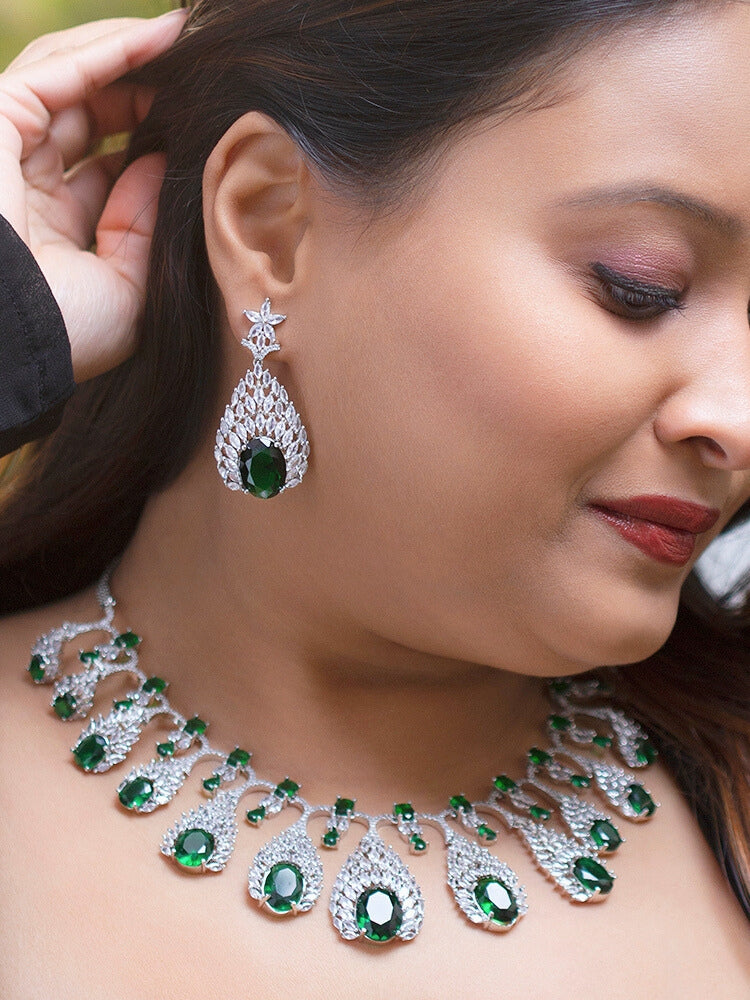 Close-up of a woman wearing an ornate Western Green Diamond Silver Collar jewellery set and earrings with American Diamond and Green Colored Stones. A woman wearing a luxury American diamond necklace set styled beautifully for a wedding guest look in India. Elegant wedding jewelry look featuring a premium artificial American diamond necklace.