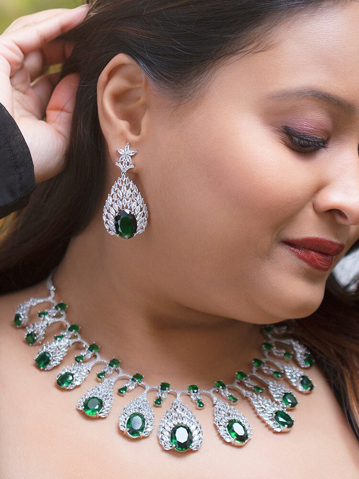 Close-up of a woman wearing an ornate Western Green Diamond Silver Collar jewellery set and earrings with American Diamond and Green Colored Stones. A woman wearing a luxury American diamond necklace set styled beautifully for a wedding guest look in India. Elegant wedding jewelry look featuring a premium artificial American diamond necklace.