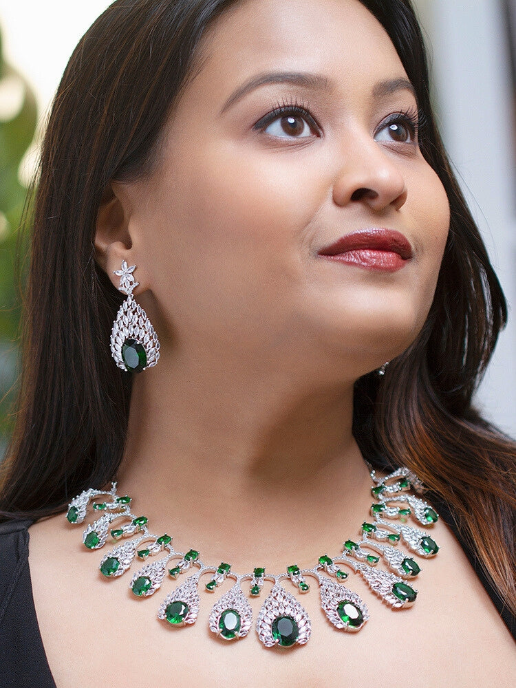 Close-up of a woman wearing an ornate Western Green Diamond Silver Collar jewellery set and earrings with American Diamond and Green Colored Stones. A woman wearing a luxury American diamond necklace set styled beautifully for a wedding guest look in India. Elegant wedding jewelry look featuring a premium artificial American diamond necklace.