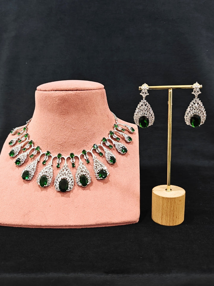Close-up of an ornate Western Green Diamond Silver Collar jewellery set and earrings with American Diamond and Green Colored Stones. A luxury American diamond necklace set styled beautifully for a wedding guest look in India. Elegant wedding jewelry look featuring a premium artificial American diamond necklace.