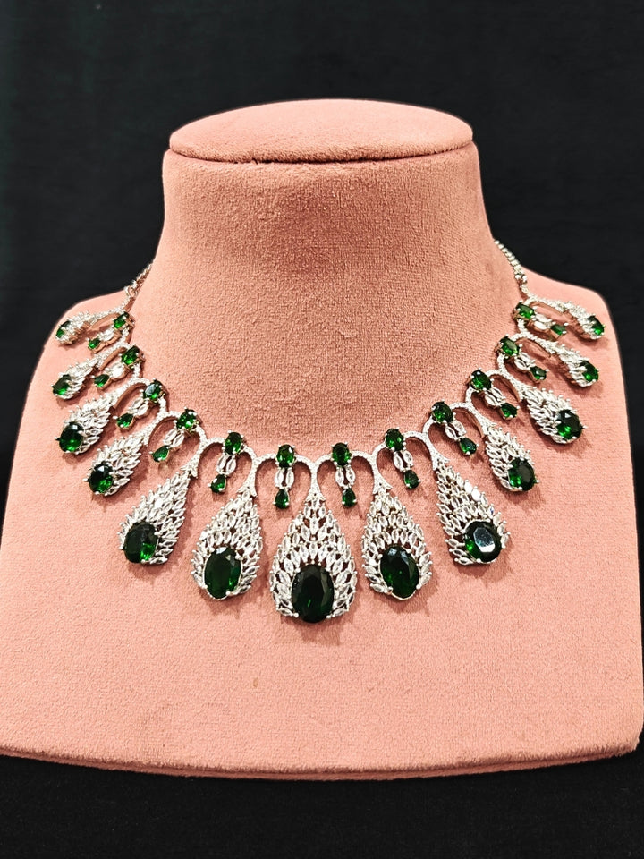 Close-up of an ornate Western Green Diamond Silver Collar jewellery set and earrings with American Diamond and Green Colored Stones. A luxury American diamond necklace set styled beautifully for a wedding guest look in India. Elegant wedding jewelry look featuring a premium artificial American diamond necklace.