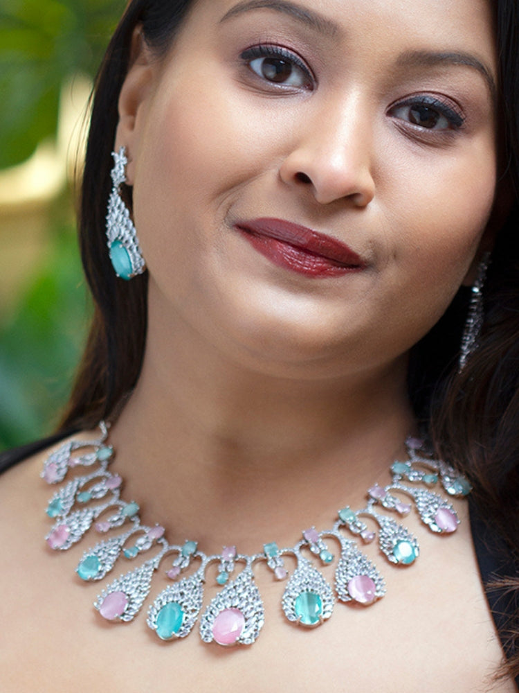 Close-up of a woman wearing an ornate Western Pink & Green Diamond Silver Collar jewellery set and earrings with American Diamond and Colored Stones. A woman wearing a luxury American diamond necklace set styled beautifully for a wedding guest look in India. Elegant wedding jewelry look featuring a premium artificial American diamond necklace.