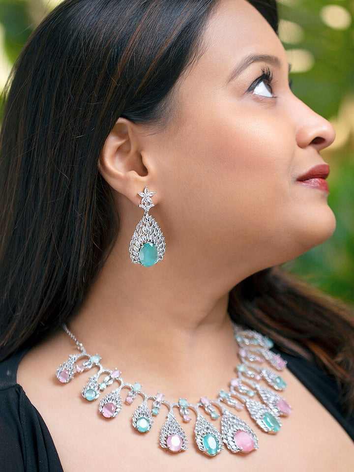 Close-up of a woman wearing an ornate Western Pink & Green Diamond Silver Collar jewellery set and earrings with American Diamond and Colored Stones. A woman wearing a luxury American diamond necklace set styled beautifully for a wedding guest look in India. Elegant wedding jewelry look featuring a premium artificial American diamond necklace.