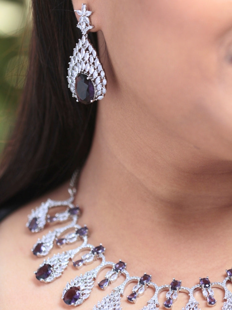 Close-up of a woman wearing an ornate Western Purple Diamond Silver Collar jewellery set and earrings with American Diamond and Purple Colored Stones. A woman wearing a luxury American diamond necklace set styled beautifully for a wedding guest look in India. Elegant wedding jewelry look featuring a premium artificial American diamond necklace.