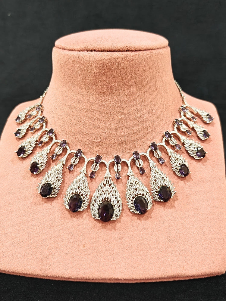 Close-up of an ornate Western Purple Diamond Silver Collar jewellery set and earrings with American Diamond and Purple Colored Stones. A luxury American diamond necklace set styled beautifully for a wedding guest look in India. Elegant wedding jewelry look featuring a premium artificial American diamond necklace.
